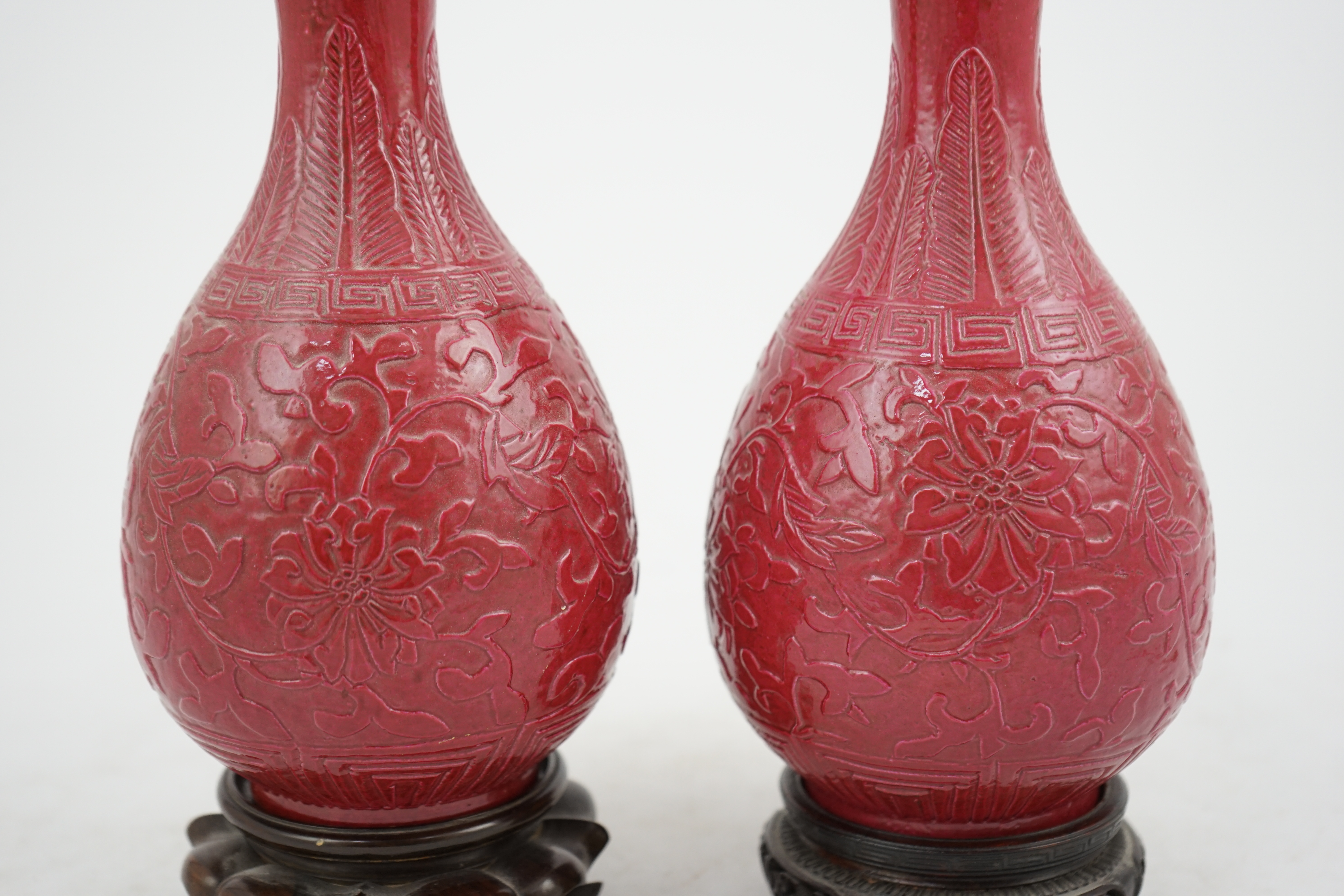 A pair of Chinese ruby ground ‘lotus’ bottle vases, late 19th century, each carved in relief with lotus flowers, scrolling tendrils and leaves, both with carved stands, 24cm high. Condition - one vase the neck broken bot